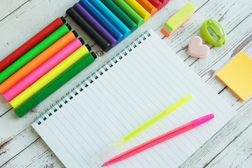 An open notebook, colorful bright markers, pens, sharpener, eraser, stickers and clay on a wooden background...