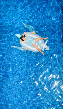 Overhead view of girl lying on unicorn shaped float in swimming pool