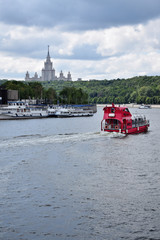 Moscow, Russia - July 8, 2019: Red pleasure boat on the Moskva river. The view from the Berezhkovskaya embankment. Sparrow Hills and Moscow State University in the background