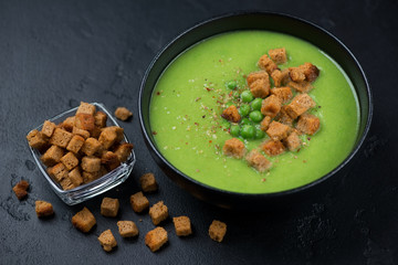 Bowl of green peas cream-soup with croutons over black stone background, studio shot