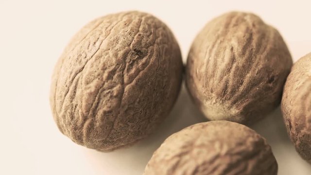 Myristica fragrans, whole nutmegs on white table. Slow pan, closeup, macro shot. Switching selective focus.