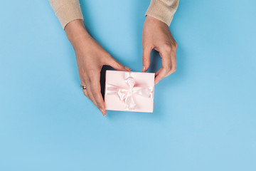 Fototapeta na wymiar Womans hands holding gift or present box on blue pastel table. Flat lay for birthday or New Year.