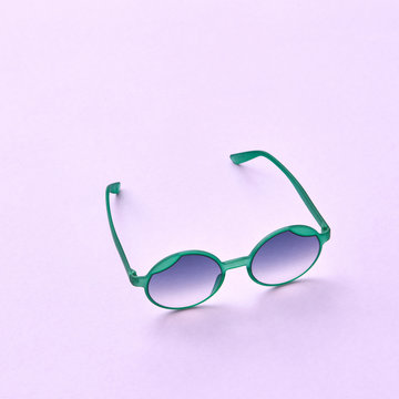 Plastic green sunglasses with blue mirror lenses on a pink paper background.