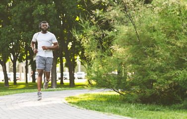 Sporty afro guy with headset is running in the park