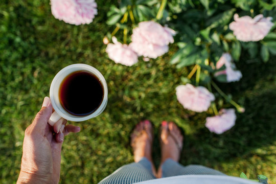 woman holding a cup of coffee early in the morning in a peony garden