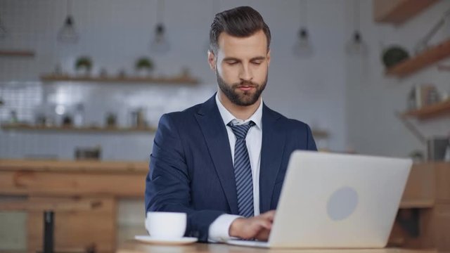 partial view of waitress giving payment terminal to handsome businessman using laptop in cafe