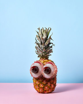 A man's face made from tropical fruits - pineapple and the eye of half of lychee with a brown bone on a duotone background.