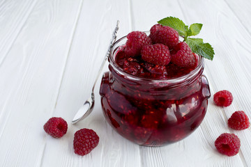 Raspberry  jam in the glass jar on the  white wooden  background. Closeup.