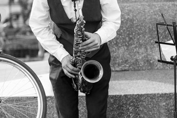 Street musician's hands playing saxophone in an urban environment. Black and white picture.