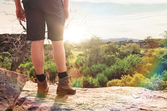 man looking out from a clifftop over a flat Australian landscape, with sun flare