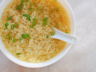 Egg drop soup also known as egg flower soup made of beaten eggs drizzled in homemade chicken broth with scallion greens. Top view of soup in white bowl.
