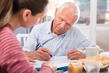 Unhappy senior woman signing documents and talking with daughter