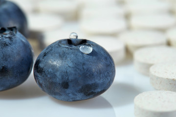 Naklejka na ściany i meble Three ripe blueberries on a background of tablets spread out on a light surface. Concept: natural vitamins. Close up.