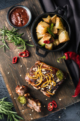 Grilled pork ribs in tomato sauce with chili pepper on a dark wooden Board and baked potatoes in a bowl