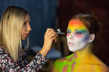 The artist puts a face painting on a lovely young model.