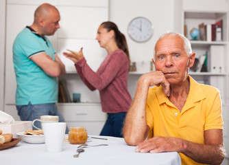 Elderly man sitting at table, unhappy family couple quarrelling