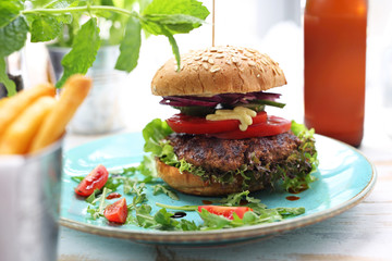 Classic homemade burger with a grilled beef cutlet, tomato, cucumber, lettuce and sauce served on a plate.