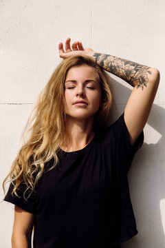 Beautiful woman standing near wall with closed eyes