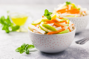 Detox turnip, carrot, apple salad in bowls with olive oil dressing. Selective focus, space for text.