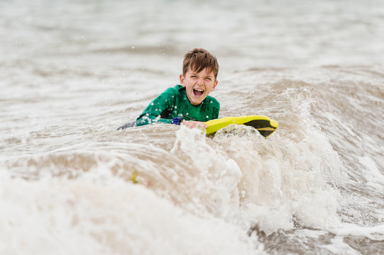 Boy wearing wetsuit learns how to bodyboard in the English sea