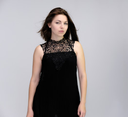 A portrait above the knee of a pretty beautiful fashionable adult brunette girl in a black dress on a white background. Standing right in front of the camera, showing different poses and emotions.