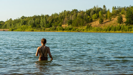 Beautiful woman in a bikini goes swimming in a lake on sunset