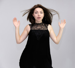 A portrait above the knee of a pretty beautiful fashionable adult brunette girl in a black dress on a white background. Standing right in front of the camera, showing different poses and emotions.