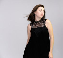 Fototapeta premium A portrait above the knee of a pretty beautiful fashionable adult brunette girl in a black dress on a white background. Standing right in front of the camera, showing different poses and emotions.