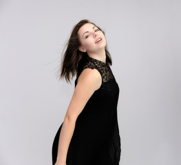 Fototapeta premium A portrait above the knee of a pretty beautiful fashionable adult brunette girl in a black dress on a white background. Standing right in front of the camera, showing different poses and emotions.