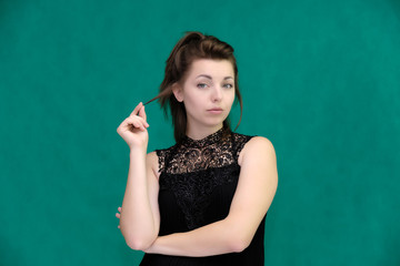 Portrait of a pretty beautiful fashionable adult brunette girl in a black dress on a green background. Standing right in front of the camera, showing different poses and emotions.