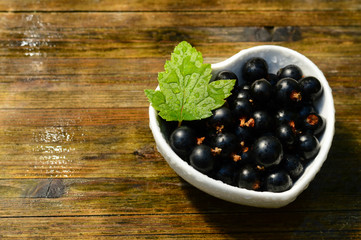 blackcurrant harvest in a ceramic heart shaped bowl on a wet wooden table