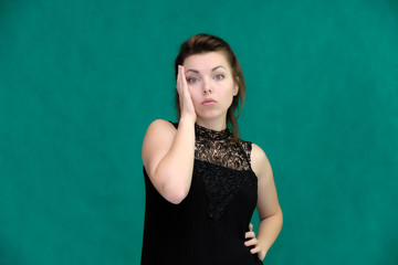 Portrait of a pretty beautiful fashionable adult brunette girl in a black dress on a green background. Standing right in front of the camera, showing different poses and emotions.