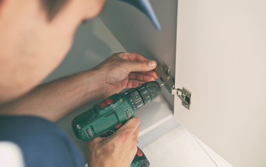 The carpenter is assembling the kitchen and works with screwdriver
