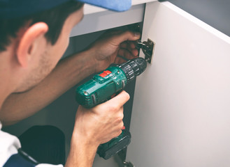 The carpenter is assembling the kitchen and works with screwdriver