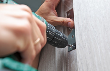 The man is installing the part of the wooden door by the screwdriver