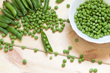 Background with freshness green peas scattered on the light wooden table and collected in white bowl
