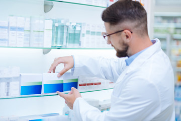 Attentive apothecary putting medicine in order on shelves