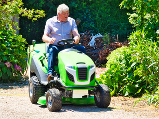 Senior man driving a tractor lawn mower in garden with flowers