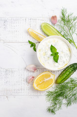 Greek dip sauce or dressing tzatziki and ingredients decorated with olive oil and mint on white wooden table Top view Flat lay Copy space