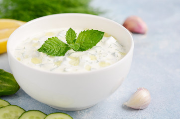 Greek dip sauce or dressing tzatziki decorated with olive oil and mint on blue background