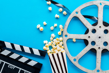 Filmmaker profession with clapperboard, popcorn and video tape on blue background top view copyspace