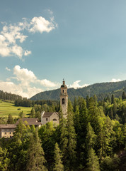 Fototapeta na wymiar Old church on a wooded mountain at blue sky in the Swiss Alps
