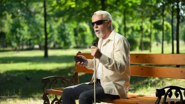 Sad blind man holding phone without voice app, inappropriate gadget for impaired