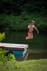 Childhood summer fun boy jumping off dock into pond