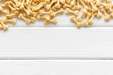 Dry puppy food in shape of bone on white wooden background top view copyspace