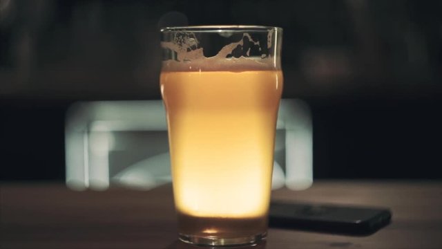 Glass of craft fresh draft beer stands on the table and glows yellow. Shallow depth of field. Blurred background. Slow motion