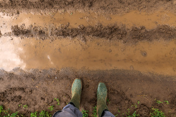 Farmer in rubber boots standing on muddy dirt road
