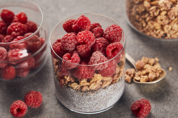 selective focus of tasty yogurt with raspberries, oat flakes and chia seeds near teaspoon on marble surface