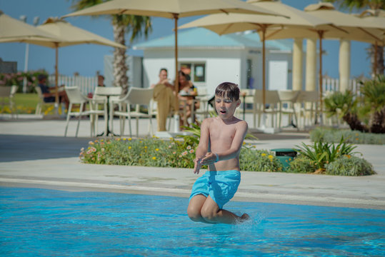 European boy jumping into swimming pool at resort. Moment of entrance in water.