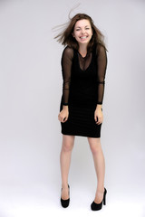 Fototapeta premium Horizontal Portrait of a pretty slim beautiful fashionable adult girl with beautiful brunette hair in a black dress. It should be in full growth, talking showing different poses and emotions